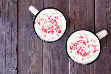 Two cups of Christmas hot chocolate with candy cane sprinkles. Overhead view on a dark wood...