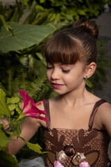 Niña pequeña oliendo una flor rosa vestida de danza clásica ballet en un jardín verde con una...