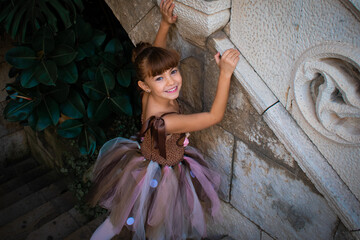Niña pequeña bailando ballet en un jardín con muros románicos de piedra con poses de danza...