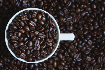 Cup with coffee beans  on roasted coffee beans as background.