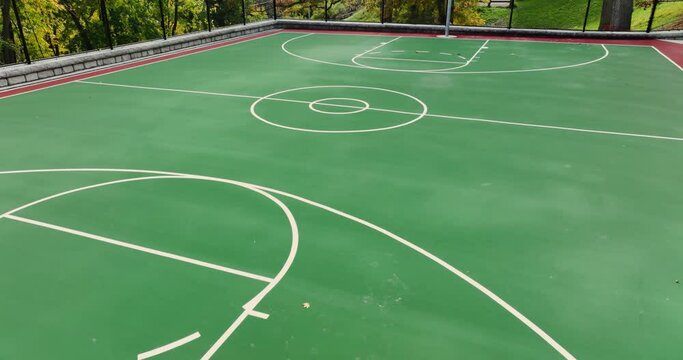Aerial video of a new green and red outdoor basketball court at school playground or part.  Court includes retaining walls and black vinyl coated chain link fence.	