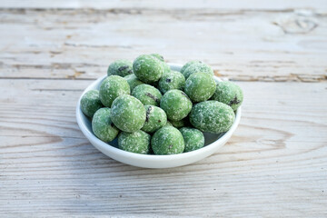 Wasabi nuts lie in a white porcelain bowl on a wooden surface