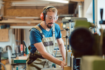 Absorbed carpenter with ear protection and safety goggles at the milling machine working on wood