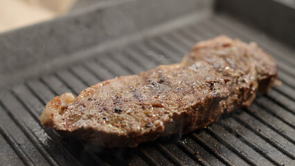 frying new york steak with tongs on grill pan