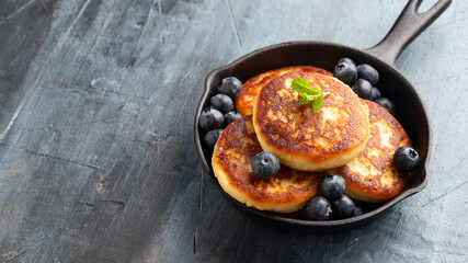 Cottage cheese pancakes served in cast iron frying pan with blueberries and mint leaves. Healthy breakfast food.