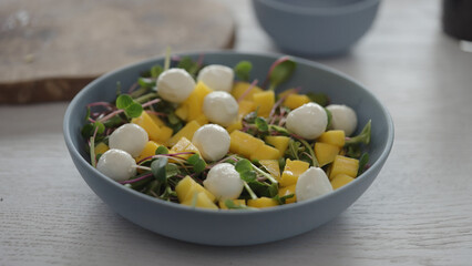 salad with mango, mozzarella and micro greens in blue bowl