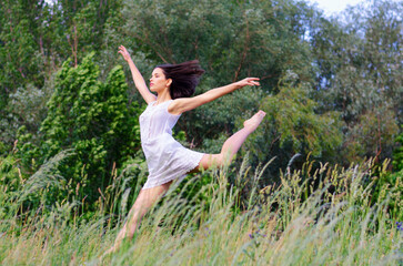 Young woman in white dress jumping and dancing in the nature on a beautiful summer day