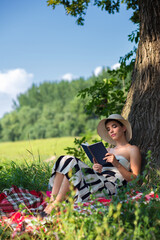 Young beautiful elegant woman reading book on the sunny summer meadow