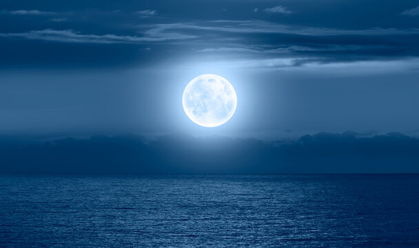Night sky with moon in the dark clouds and darkblue sea in the foreground "Elements of this image furnished by NASA"