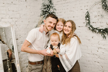 Father, mother hugs son and daughter stand near Christmas tree at home. Mom, dad with kids. Happy New Year and Merry Christmas. Christmas decorated interior. The concept of family holiday. Closeup.