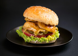 Close-up of a delicious fresh homemade burger with lettuce, cheese, onion and tomato on a rustic wooden board on a dark background