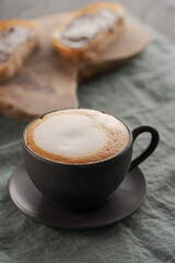 Cappuccino in black cup with ciabatta slices with chocolate spread on background