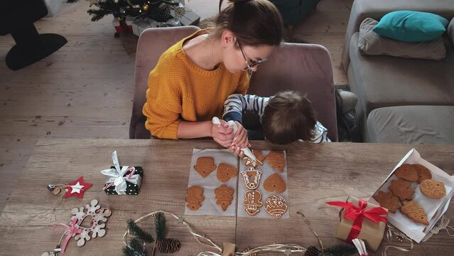 Mother and child decorating Christmas gingerbread cookies with icing sugar together top view