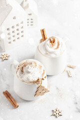 Two Mugs of hot chocolate or cocoa with whipped cream and cinnamon on white marble background with bokeh lights . Xmas mock up, card with text space. Traditional Christmas or New Year drinks.