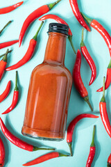 Hot chili sauce in a bottle on a bright blue background with fresh red pepper. The concept of...