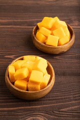 Dried mango cubes in wooden bowls on brown wooden, side view.