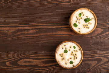 Yoghurt with granadilla and mint in wooden bowl on brown wooden, top view, copy space.