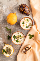 Yoghurt with granadilla and mint in clay bowl on brown concrete, top view.