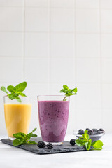 Purple and yellow fruit smoothies or milkshakes with blackberry and mint on gray concrete background. The concept of healthy, detox and dietary nutrition.