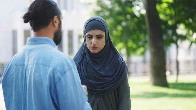 Angry Muslim man scolding upset wife in hijab outdoors, abusive relationship