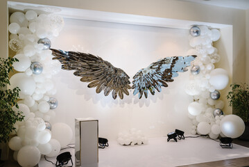 Photo zone with angel wings on the background of balloons. Photo area in silver style. Baby shower,...