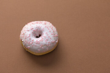 Ciambella con glassa e zuccherini rosa su superficie marrone
