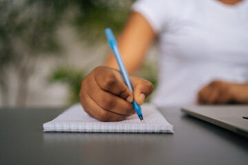 Close-up hands of unrecognizable African-American woman writing down important work information in...