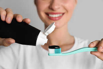 Woman applying charcoal toothpaste onto brush on grey background, closeup