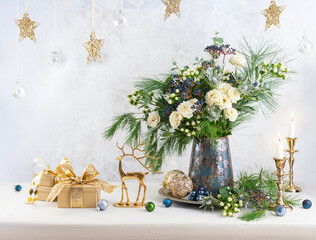 Christmas decorations, candles, gift boxes and flower bouquet. Winter arrangement with roses, fir branches, winter berries. Christmas still life.
