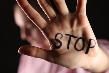 Woman with word Stop written on hand against dark background, closeup. Domestic violence concept