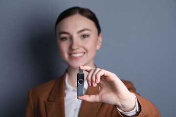 Woman holding usb flash drive on grey background, closeup