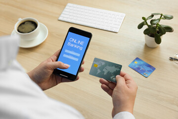 Man using online banking app on smartphone and credit card at wooden office table, closeup