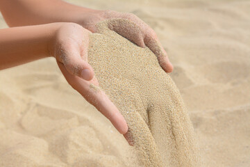 Child pouring sand from hands on beach, closeup. Fleeting time concept