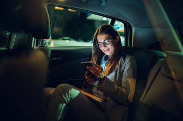 Business woman using smartphone while sitting in a backseat of a car at night
