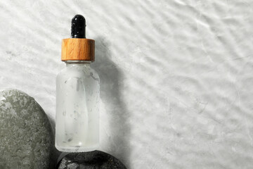 Bottle of face serum and spa stones in water on light background, flat lay. Space for text