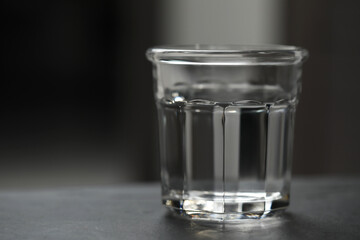 Glass of pure water on black table against blurred background, space for text