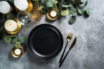 Christmas table setting at stone table. Black plate, cutlery, candles and golden decorations.