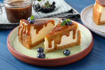 Pieces of delicious caramel cheesecake with blueberry and mint on blue wooden table