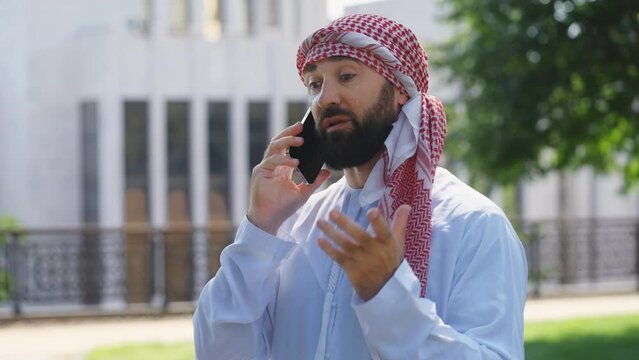 Arab businessman in traditional white dress talking on phone, business call