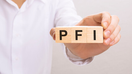 Fototapeta na wymiar hand holding wood cubes with PFI text. financial, management, economic and business concept