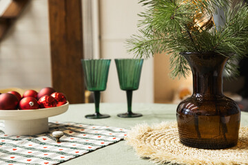 Christmas decor on the table. Vase with fir branches and glasses with lights on the background