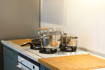 Shiny cooking pot and frying pans on stove on a wooden table light kitchen.