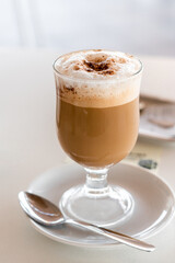 Cappuccino coffee in glass cup on white plate