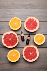 Bottles of citrus essential oils and fresh fruits on wooden table, flat lay