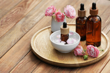 Fototapeta na wymiar Bottles of rose essential oil and flowers on wooden table, space for text