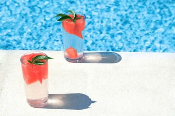 Refreshing watermelon drink in glasses near swimming pool outdoors. Space for text