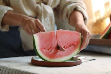Woman cutting slice of fresh watermelon at wooden table, closeup