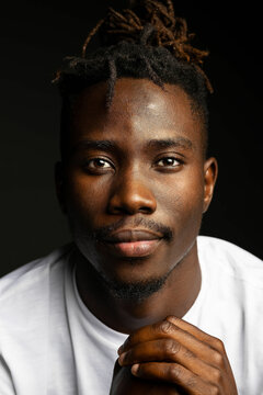 Dark studio portrait of black man in white shirt staring at camera
