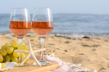 Glasses with rose wine and snacks on sandy seashore. Space for text