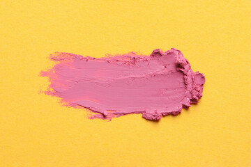 Smear of bright lipstick on yellow background, top view